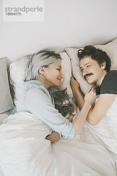 Smiling woman embracing man lying on bed at home