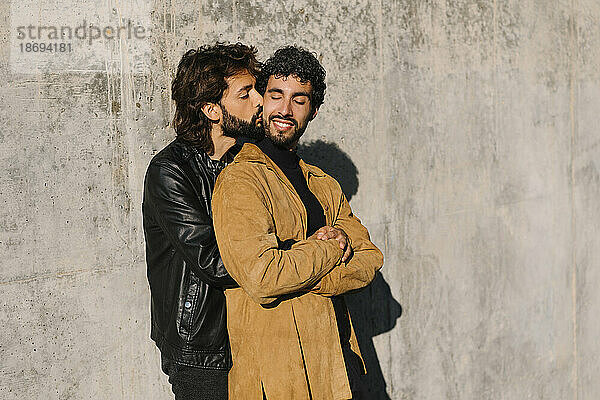 Schwuler Mann küsst Freund an sonnigem Tag in der Nähe einer Betonmauer