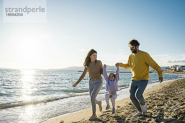 Vater und Mutter spielen mit Tochter am Strand am Meer
