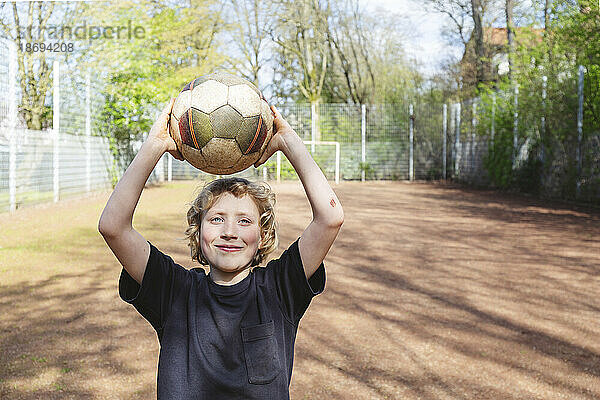 Lächelnder Junge hält Fußball auf dem Spielplatz