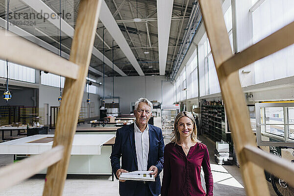 Lächelnde Geschäftsfrau und Geschäftsmann betrachten Holzkonstruktion in der Fabrik