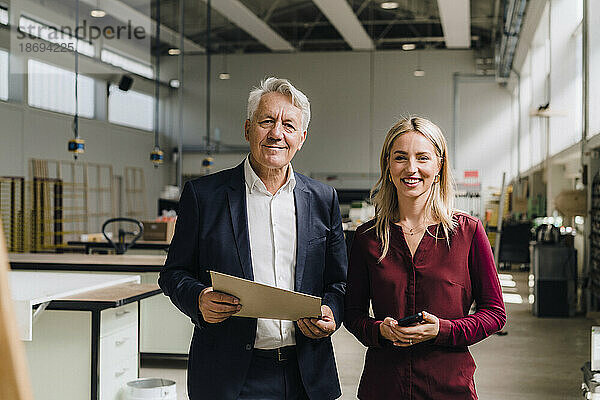 Lächelnder Kollege mit leitendem Geschäftsmann  der Dokument in der Fabrik hält