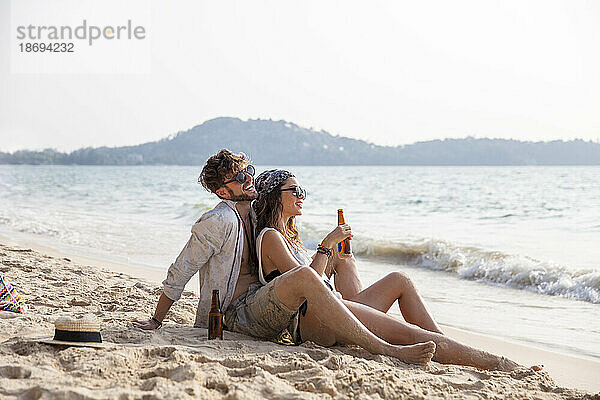 Glückliches Paar genießt Getränke im Sand am Strand