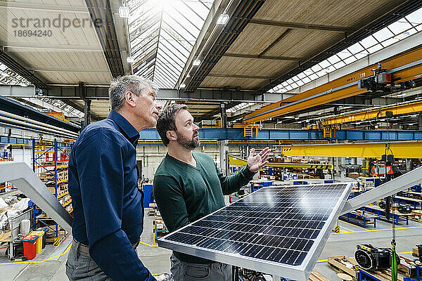 Geschäftsleute mit Solarpanel diskutieren in der Fabrik