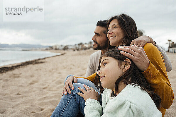 Glückliche Frau und Mann sitzen mit Tochter am Strand