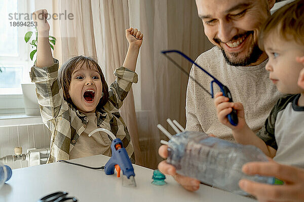 Cheerful boy with father and brother making plastic car bottle at home