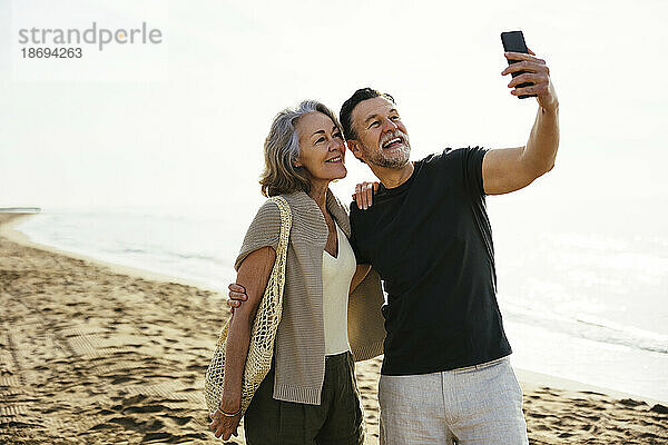 Mann macht Selfie mit Frau  die am Strand steht