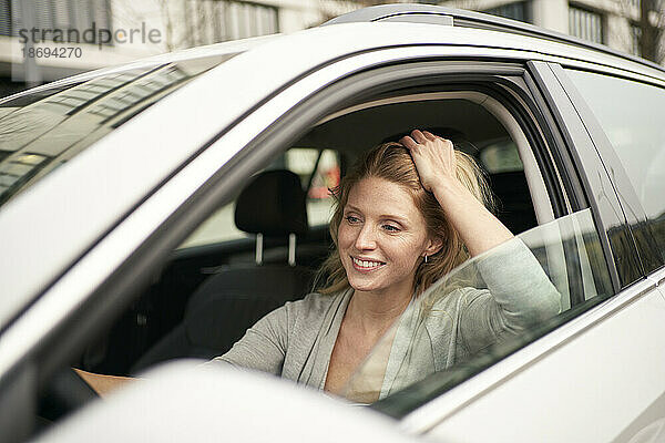 Lächelnde Frau mit der Hand im Haar  die Auto fährt