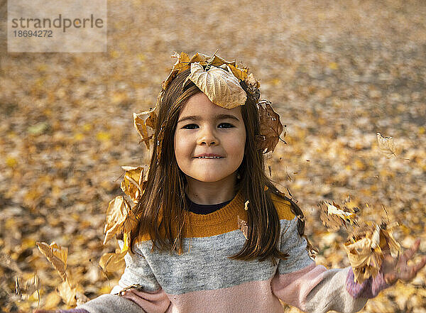 Lächelndes Mädchen bedeckt mit trockenen Blättern im Herbstpark