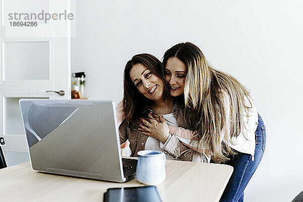 Tochter umarmt Mutter mit Laptop zu Hause