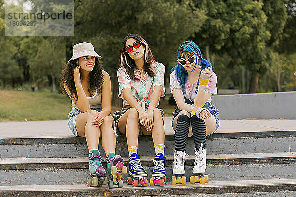 Lächelnde junge Freunde sitzen auf der Treppe im Park