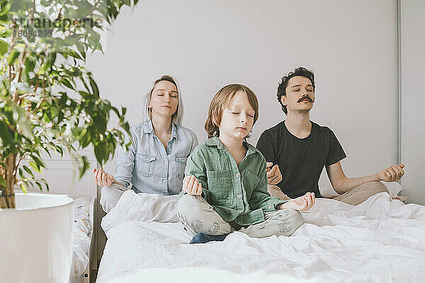 Family meditating on bed at home