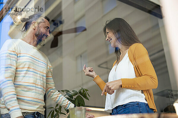 Glückliches Paar steht und redet im Café  gesehen durch die Glasscheibe