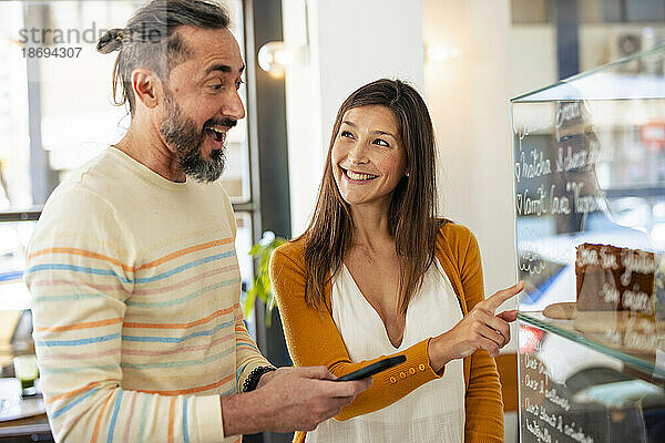 Lächelnde Frau zeigt auf die Essensauslage eines Mannes im Café