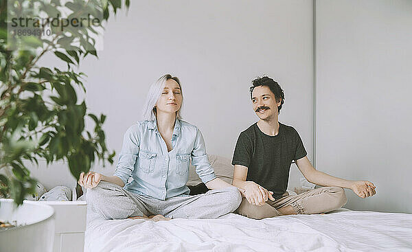 Lächelnder Mann und Frau machen Yoga zu Hause im Bett