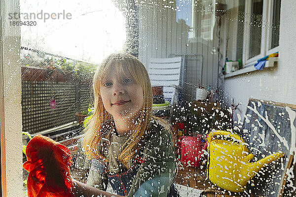 Lächelndes rothaariges Mädchen  das Fensterglas abwischt