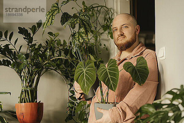 Bearded man holding potted plants at home