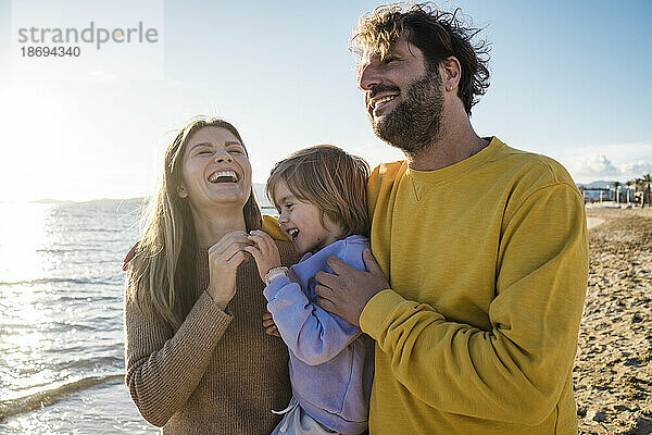 Woman laughing by daughter and man at beach