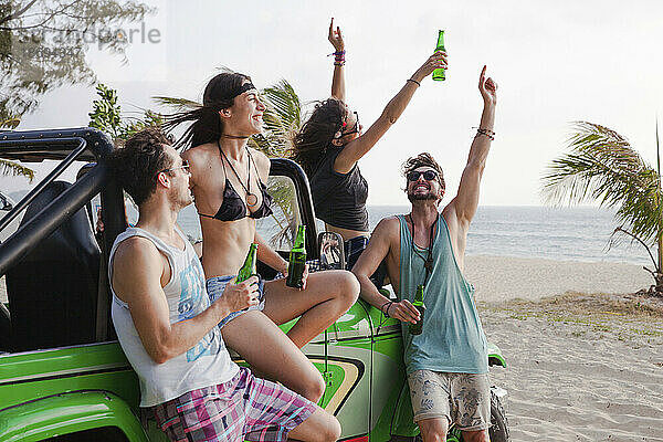 Fröhliche Freunde genießen Drinks mit Geländewagen am Strand