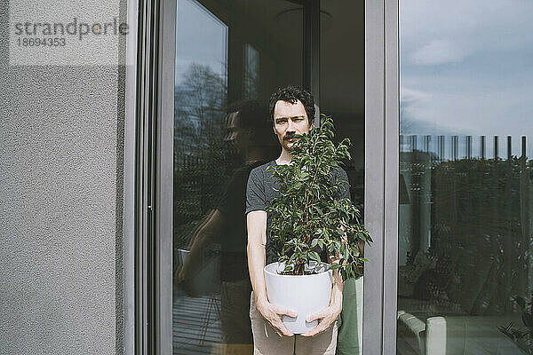 Mann hält Topfpflanze vor Glastür