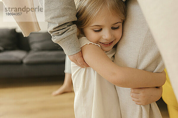 Lächelndes Mädchen umarmt das Bein der Großmutter zu Hause