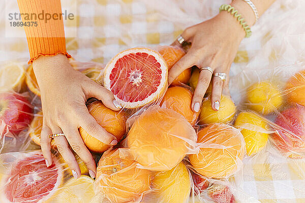 Hände einer Frau berühren frische Zitrusfrüchte auf einem mit Plastikfolie bedeckten Tisch