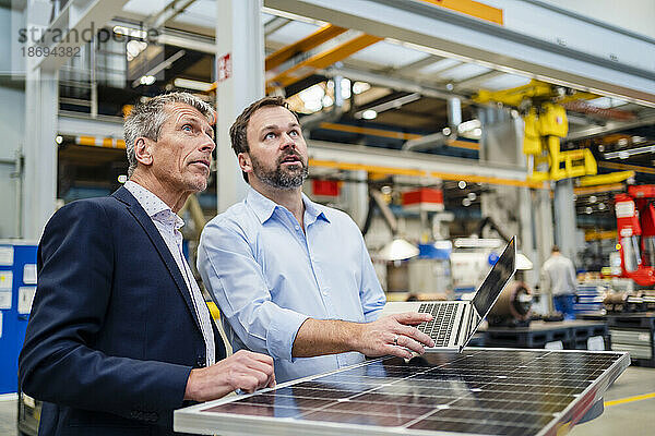Manager und Geschäftsmann schauen durch Solarpanel in der Fabrik nach oben