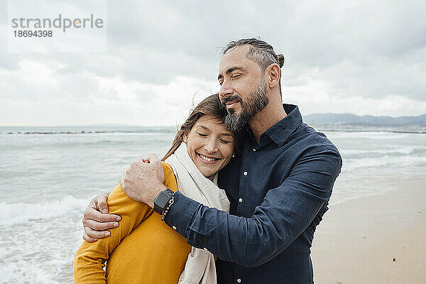 Lächelnder reifer Mann umarmt Frau am Strand