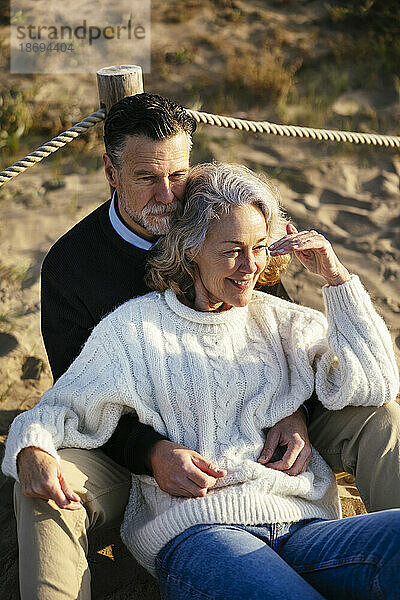Mann sitzt mit Frau und schützt die Augen am Strand
