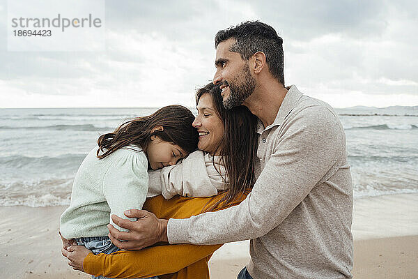 Lächelnder Mann und Frau tragen und umarmen ihre Tochter am Strand