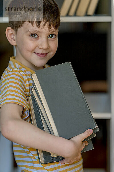 Lächelnder Junge hält einen Stapel Bücher zu Hause