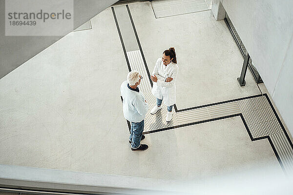 Junger Arzt diskutiert mit einem älteren Kollegen  der in der Lobby des Krankenhauses steht