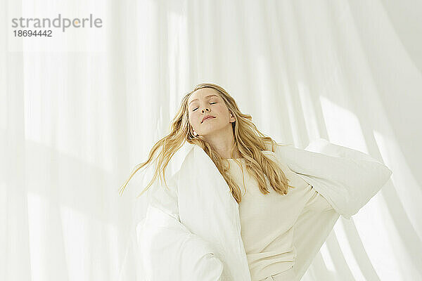 Blonde Frau mit geschlossenen Augen  in eine Decke gehüllt  vor einem durchscheinenden Vorhang