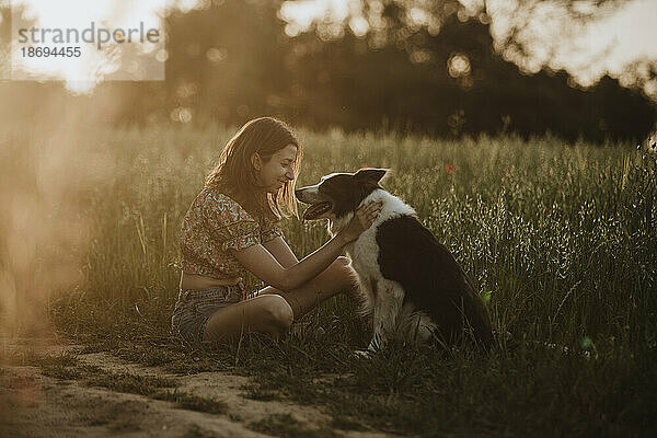 Lächelnde Frau sitzt mit Border-Collie-Hund im Feld