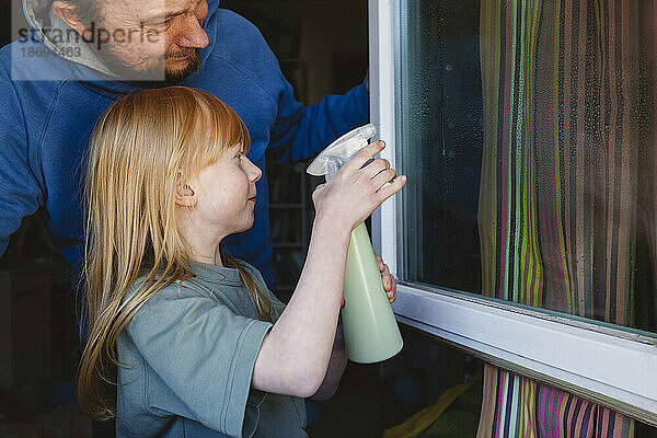 Mädchen putzt Fenster mit Vater zu Hause