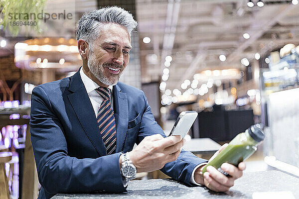 Lächelnder Geschäftsmann fotografiert eine Smoothie-Flasche im Café