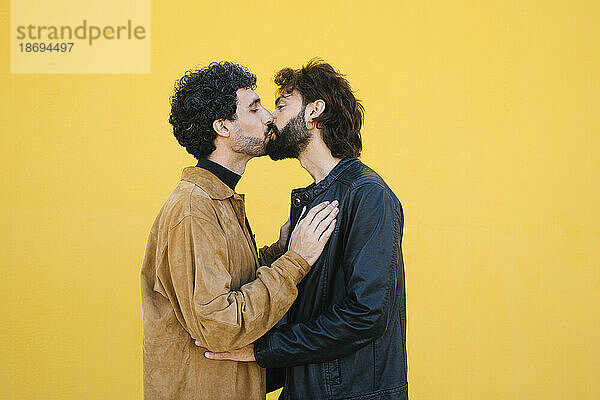 Romantic gay couple kissing each other against yellow background