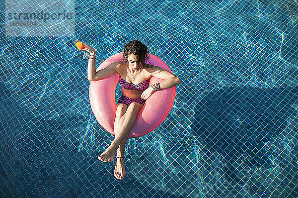 Frau hält an sonnigem Tag ein Getränk im Schwimmbad