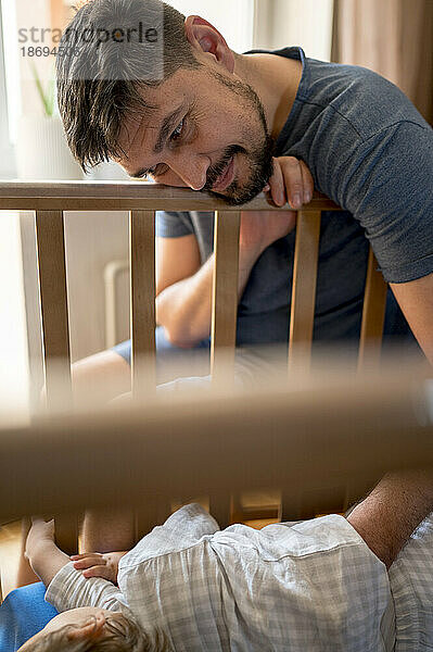 Father putting son to sleep in crib at home