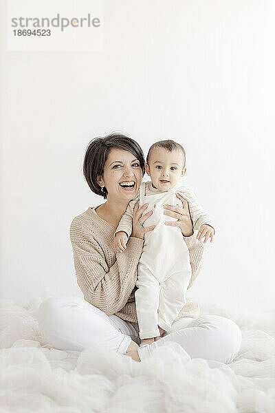 Glückliche Frau sitzt mit süßem Sohn vor weißer Wand