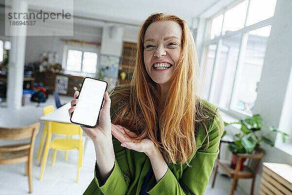 Glückliche Geschäftsfrau zeigt Smartphone-Bildschirm im Büro