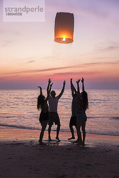 Freunde lassen brennende Papierlaternen los  die bei Sonnenuntergang am Strand stehen