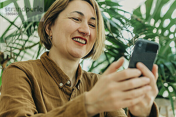 Lächelnde Frau benutzt Mobiltelefon im Café