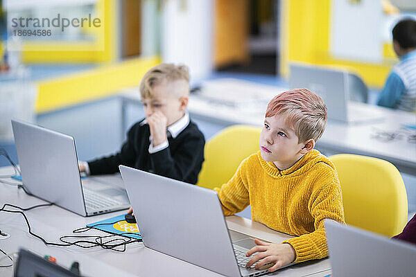Boy day dreaming sitting with laptop in class at school
