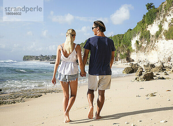 Happy young couple holding hands and walking at beach