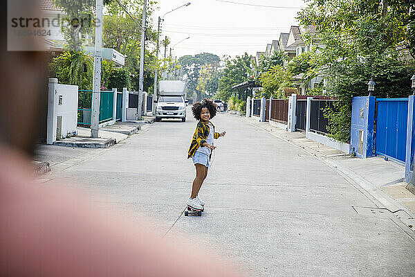Lächelndes Mädchen  das auf Fußweg Skateboard fährt