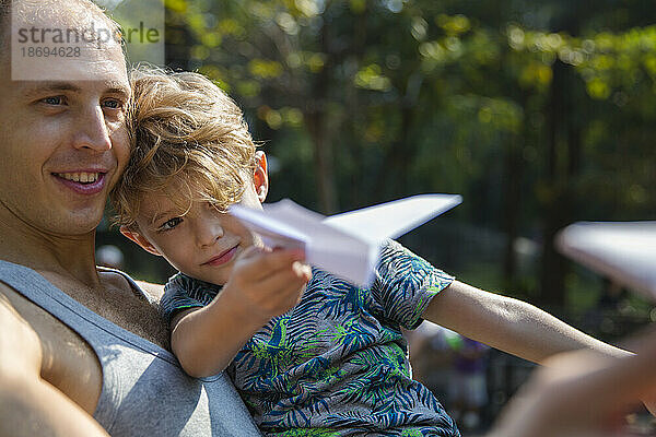 Vater und Sohn spielen an einem sonnigen Tag mit einem Papierflieger