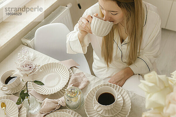 Frau trinkt schwarzen Kaffee und sitzt zu Hause am Tisch
