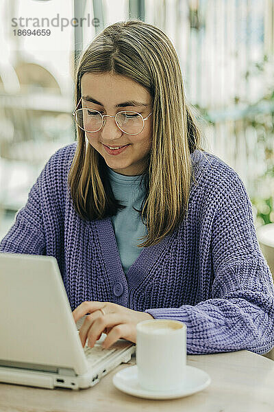 Teenager-Mädchen sitzt mit Laptop in der Schulcafeteria