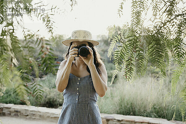Frau fotografiert mit der Kamera  die in der Nähe von Pflanzen steht
